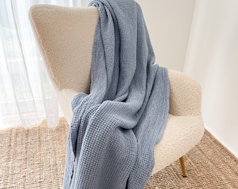 May include: A light blue waffle weave throw blanket draped over a cream-colored armchair. The chair is sitting on a woven jute rug.