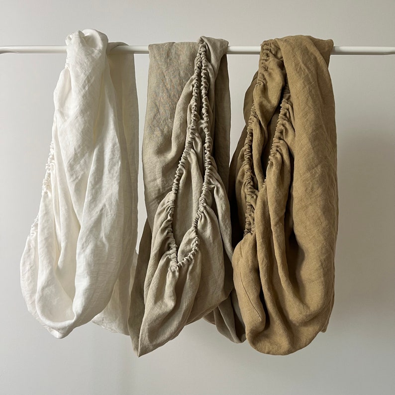 May include: Three fitted sheets in different colors: white, beige, and brown. The sheets are made of linen and have a relaxed, casual look.