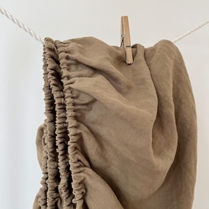 May include: A brown linen fitted sheet with elastic edging hanging on a clothesline.