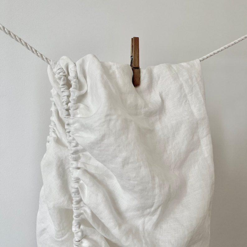 May include: White linen fitted sheet hanging on a clothesline with a wooden clothespin.