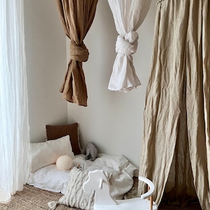 May include: A white rocking horse with wooden rockers sits on a woven rug in a playroom. Three linen canopy tents hang from the ceiling, one white, one brown, and one beige.