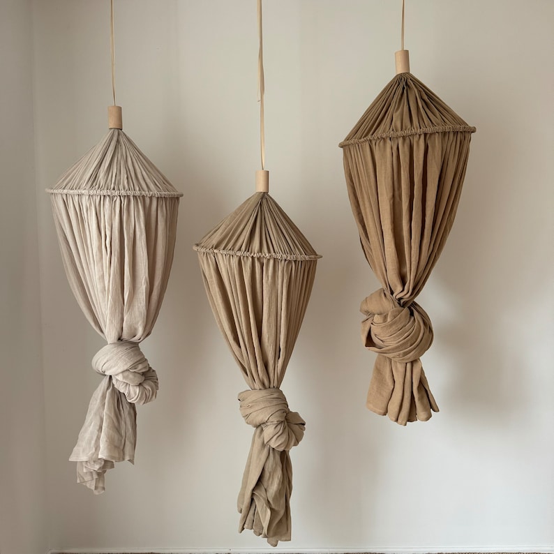 May include: Three hanging fabric canopies in beige and brown tones. The canopies are made of a soft, flowing fabric and are perfect for creating a cozy and intimate space.