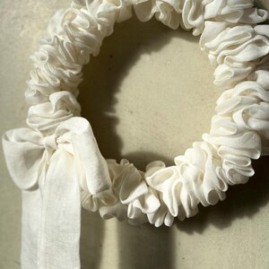 Puede incluir: Una corona de tela blanca con un gran lazo blanco. La corona est&aacute; hecha de tela fruncida y es perfecta para un estilo de decoraci&oacute;n r&uacute;stico o de granja.