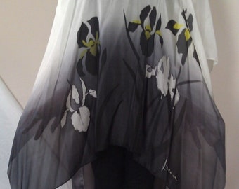 May include: A white, sheer, long-sleeved top with a black and white floral print. The top has a high, round neckline and a flowing, asymmetrical hemline. The print features stylized iris flowers with yellow accents. The top is signed "Kiova" on the bottom right side.