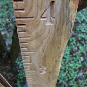 May include: A wooden growth chart with carved numbers and lines. The chart is made of natural wood with a light brown color and a visible grain pattern. The number "4" is carved into the wood.