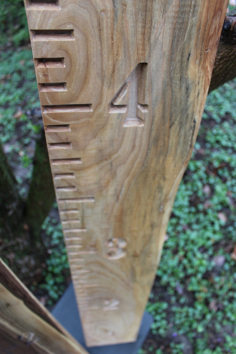May include: A wooden growth chart with carved numbers and lines. The chart is made of natural wood with a light brown color and a visible grain pattern. The number "4" is carved into the wood.