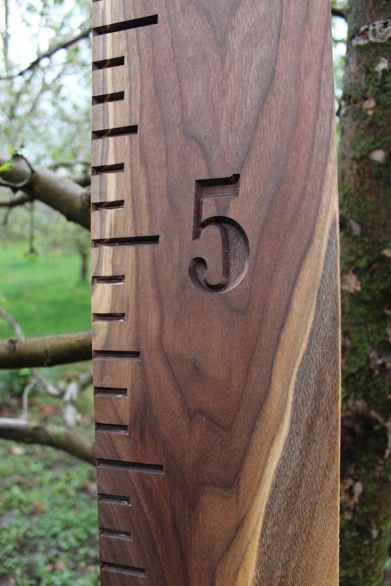 May include: A wooden growth chart with a dark brown finish. The chart has a number "5" carved into the wood. The chart is made of walnut wood.