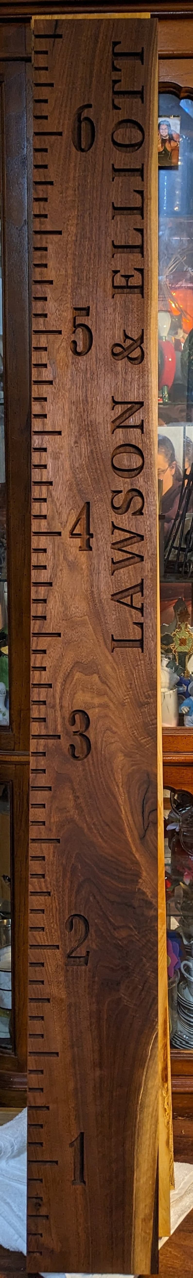 May include: A wooden growth chart with a ruler on the left side and the names "JAMISON & ELLIOT" engraved on the right side. The numbers 1 through 6 are engraved on the right side of the ruler.