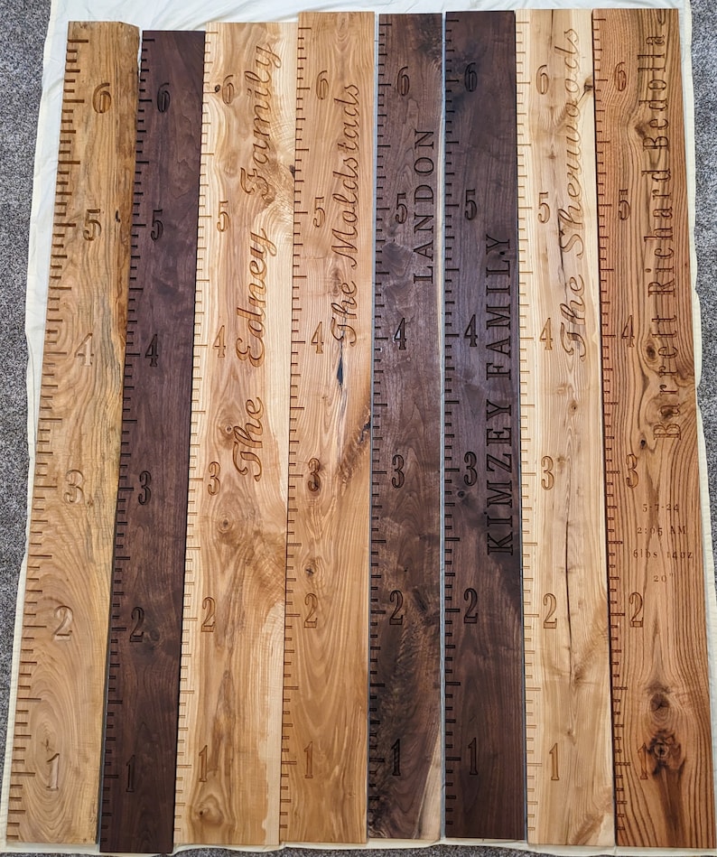May include: Seven wooden growth charts with names and measurements in inches. The charts are made of different types of wood, including walnut and oak. The names on the charts are: The Edney Family, The Moldstads, Landon, Kimzey Family, The Sherwoods, Barrett Richard Bedolla.