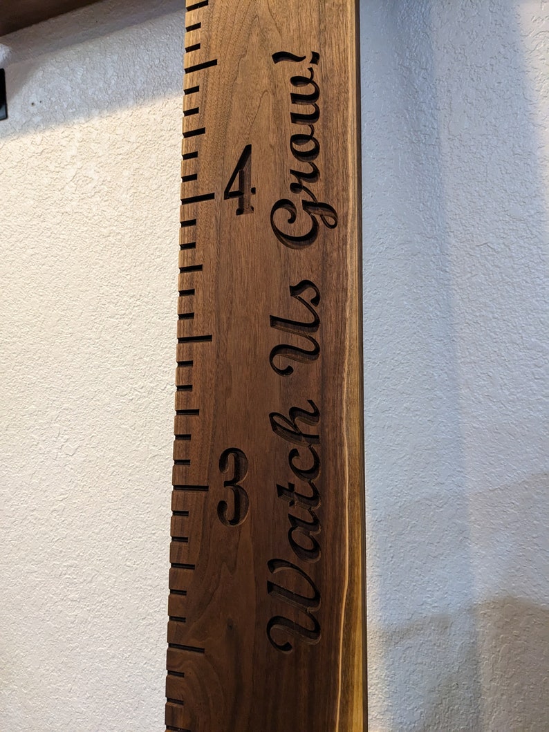 May include: A wooden growth chart with a ruler and the text "Watch Us Grow!" engraved on it. The chart is made of dark brown wood and has a natural wood grain.