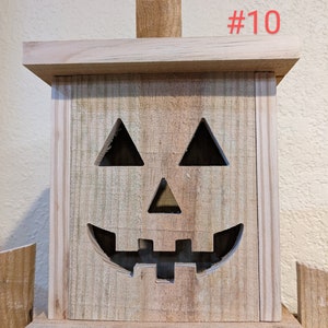 May include: A wooden jack-o'-lantern decoration with a carved face featuring triangular eyes and a smiling mouth. The pumpkin has a rectangular shape with a wooden stem and the number "#10" in red. Perfect for Halloween.