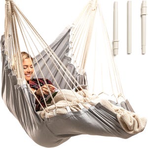 May include: A gray hammock with white ropes and a person sitting in it reading a book. The hammock is hanging from a white stand.