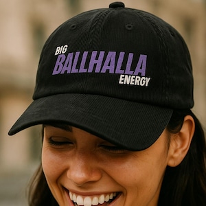 May include: Black corduroy baseball cap with the text "BIG BALLHALLA ENERGY" in purple. The cap is worn by a person smiling. The person is wearing a black tank top and has tattoos on their arms and chest.