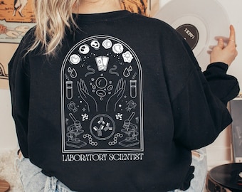 May include: Black long-sleeved sweatshirt with a white graphic design of a laboratory theme. The design includes a microscope, test tubes, cells, and the text "Laboratory Scientist".