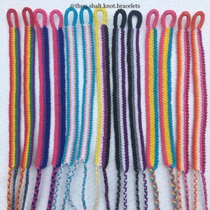 May include: A collection of 10 friendship bracelets in various colors and patterns, including rainbow, blue, pink, white, yellow, black, gray, and purple. The bracelets are made with a knotting technique and have a loop at each end. The bracelets are displayed on a white surface. @thoushalt.knot.bracelets