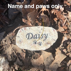 Puede incluir: Un peque&ntilde;o monumento de piedra marr&oacute;n claro con el nombre "Daisy" grabado en &eacute;l. La piedra tambi&eacute;n tiene dos huellas de patas grabadas. La piedra est&aacute; rodeada de hojas marrones.