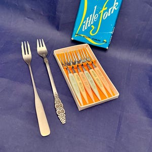 May include: A set of vintage forks, including two individual forks and a boxed set of six. The boxed set has white handles with "Miami Beach" printed on them. The box is blue with yellow text that reads "Little Fork".