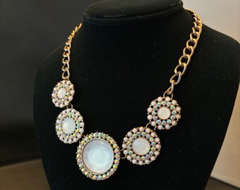 May include: A gold chain necklace with five large, round, white, iridescent, rhinestone-encrusted pendants.