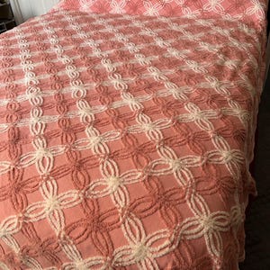 May include: A pink and white crocheted bedspread with a floral pattern. The bedspread is made of a soft, fluffy material and has a vintage look.