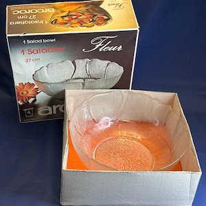 May include: A clear glass salad bowl with a flower-shaped design. The bowl is 27 cm in diameter and is in its original box. The box is white with the words "Fleur" and "1 Saladier" printed on it.