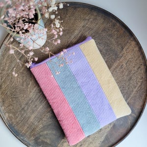 Op de afbeelding: Een gestreepte corduroy tas met roze, paarse, grijze en gele strepen. De tas ligt op een houten dienblad.