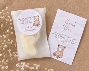 May include: A translucent favor bag containing a foot-shaped item, sealed with a round sticker featuring a brown bear and the text Thank you for coming to Chloe's baby shower. We can bearly wait. Beside it is a card with a bear and Thank You text.