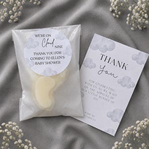 May include: A clear plastic bag containing a pale yellow wax melt, sealed with a round sticker reading WE'RE ON Cloud NINE THANK YOU FOR COMING TO ELLEN'S BABY SHOWER, alongside a rectangular card printed with THANK You FOR CELEBRATING WITH US.