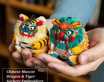 Könnte beinhalten: Ein DIY-Set zum Herstellen von bestickten chinesischen Glücksbringer-Säckchen. Das Set enthält zwei Stoffbeutel, einen in Tigerform und den anderen in Drachenform. Die Beutel sind gelb, rot, grün und weiß mit bestickten Details.