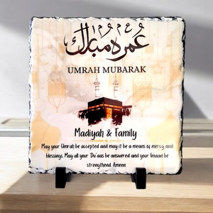 May include: A decorative stone plaque with an image of the Kaaba, a mosque in Mecca, Saudi Arabia. The plaque has the Arabic text "Umrah Mubarak" and the English text "Madiyah & Family". The plaque also has the text "May your Umrah be accepted and may it be a means of mercy and blessings. May all your Du'aas be answered and your Imaan be strengthened. Ameen."