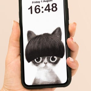 May include: Black phone case displaying a black and white illustration of a cat with a bowl-cut hairstyle. The phone screen shows the date "Friday 1 August" and the time "16:48". The phone is held in a hand.