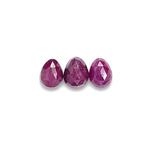May include: Three faceted ruby gemstones in a pear shape. The gemstones are a deep red color and are arranged in a row.
