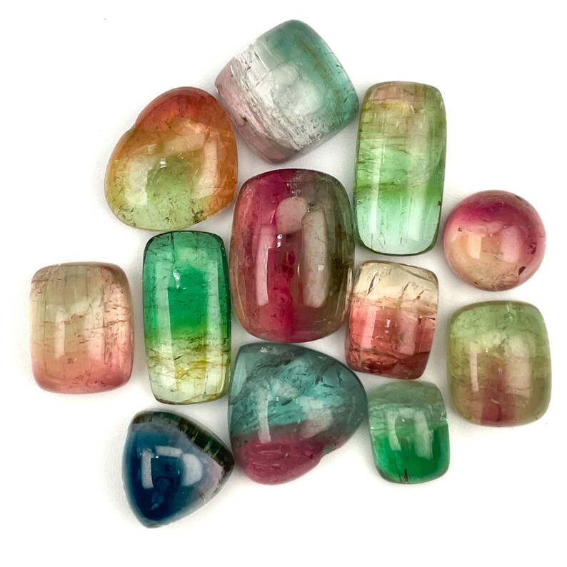 Multiple bicolor tourmaline gemstone cabochons.  Smooth cut cabochon stones of varying shades and sizes seen from the top, creating an array of reds, pinks, yellows, blues and greens.