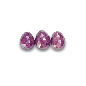 May include: Three faceted ruby gemstone beads in a teardrop shape. The beads are a deep red color with a slight purple hue.
