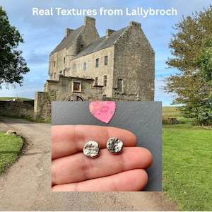 Könnte beinhalten: Ein Paar kleine, runde, strukturierte Silberohrringe. Die Ohrringe werden in einer Hand gehalten, mit einem Schloss und dem Text "Real Textures from Lallybroch" im Hintergrund.