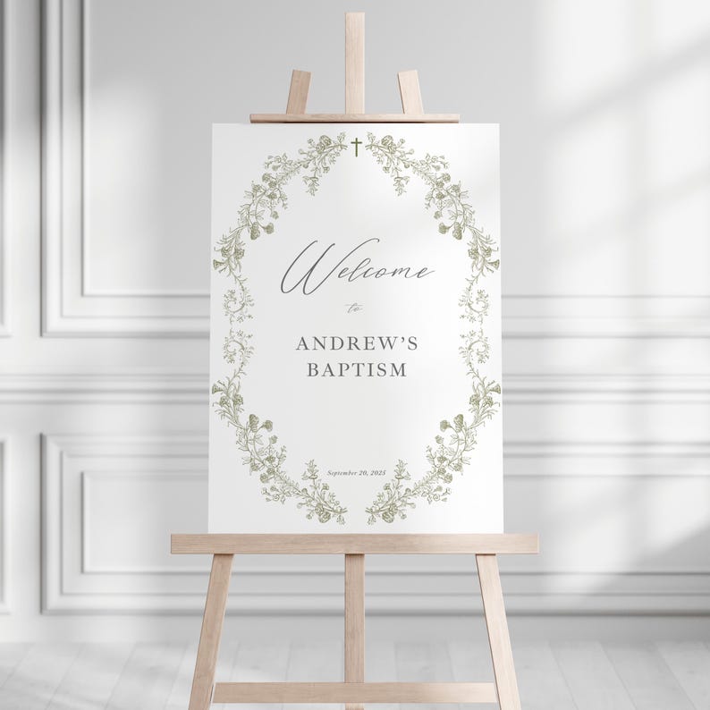 May include: A white sign on a wooden easel, with the words "Welcome to Andrew's Baptism" in a decorative font. The text is framed by a floral wreath. A small cross is at the top of the sign.