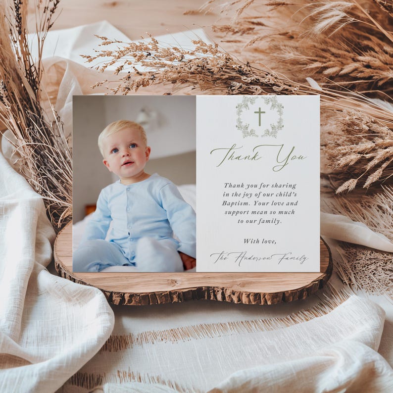 May include: A baptism thank you card with a photo of a baby in a blue outfit. The card features the text "Thank You" and a message of gratitude, along with a cross and floral design. The card is displayed on a wooden slice.