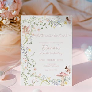 Pode incluir: Um convite rosa claro com ilustrações florais e de fadas. O texto diz "flutter and twirl" e anuncia o segundo aniversário de Elanor em 20 de outubro às 14h00. O convite inclui o endereço e o número de telefone.