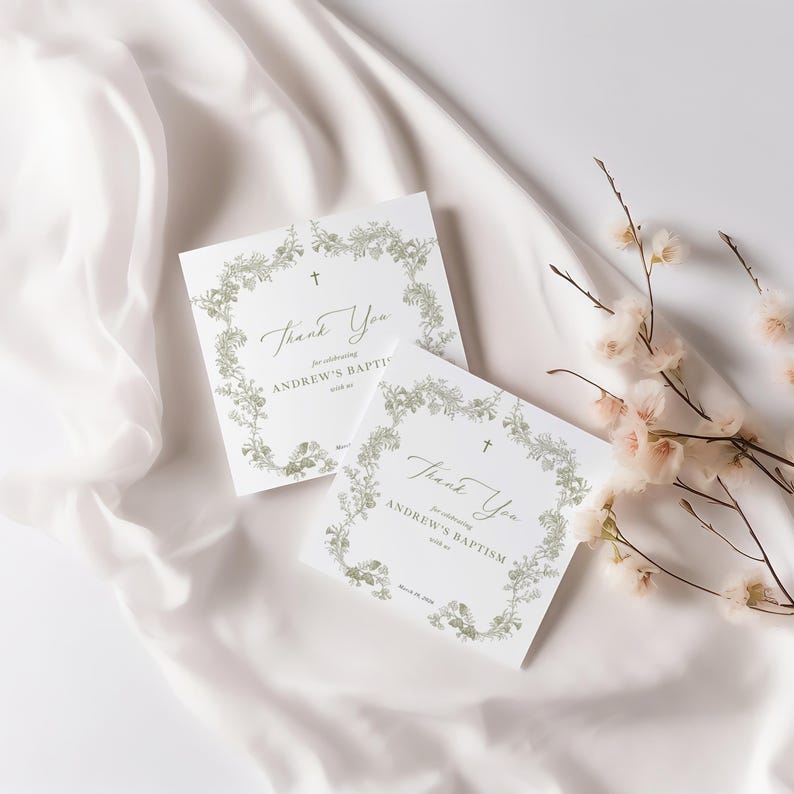 May include: Two square white cards with floral wreath borders and the words "Thank You" and "for celebrating ANDREW'S BAPTISM with us". A small cross is above the text. The cards are on a white satin surface.