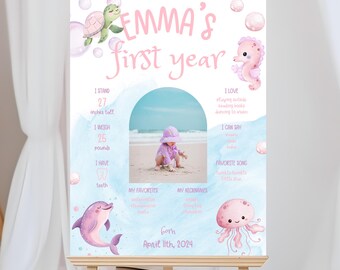 May include: A baby's first year sign with the text "EMMA'S first year". The sign includes a photo, measurements (68.58 cm tall, 11.34 kg), and illustrations of a turtle, seahorse, dolphin, and jellyfish.