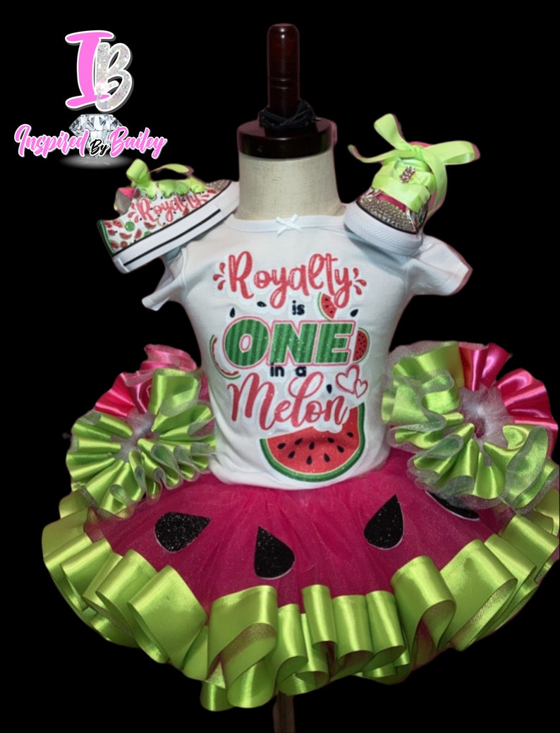 Pu&ograve; includere: Un outfit per bambina con tema anguria con una maglietta bianca che dice "Royalty is One in a Melon" e un tut&ugrave; rosa con dettagli di nastro verde. L'outfit include anche un paio di scarpe da ginnastica a tema anguria.