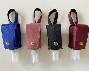 Könnte beinhalten: Vier kleine, farbenfrohe Handdesinfektionsmittelhalter. Die Halter sind in Blau, Rosa, Schwarz und Burgunderrot gehalten. Jeder Halter hat eine passende Schlaufe und einen Druckknopfverschluss. Die transparenten Desinfektionsmittelflaschen sind unten sichtbar.