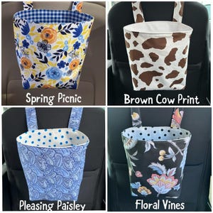 May include: Four car trash bags with different patterns. One has a blue and white gingham lining and a floral design. Another has a brown cow print. The third has a blue paisley pattern. The last has a floral vines pattern. Each bag has straps.