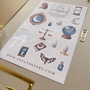 Puede incluir: Una hoja de pegatinas de tem&aacute;tica celestial con ilustraciones de lunas, estrellas, una bola de cristal, balanzas, una polilla y una vela. Las pegatinas son en tonos marrones, azules y dorados. La web www.tstationery.com est&aacute; impresa.