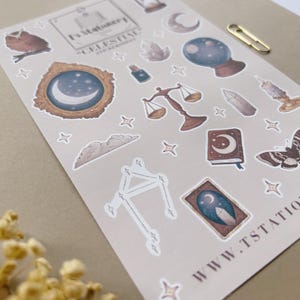 Puede incluir: Una hoja de pegatinas de tem&aacute;tica celestial con ilustraciones de un b&uacute;ho, una luna, estrellas, una balanza, una bola de cristal y un libro. Las pegatinas son en tonos marrones, azules y dorados. El texto "Celestial Sticker Sheet" es visible.