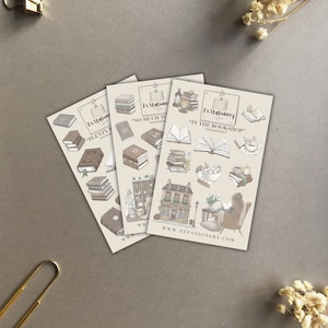 Peut inclure: Trois feuilles d'autocollants illustrant des livres, des tasses à café et une librairie. Les autocollants sont beiges et bruns avec le texte "T's Stationery" et "So Much To Read" sur les feuilles.