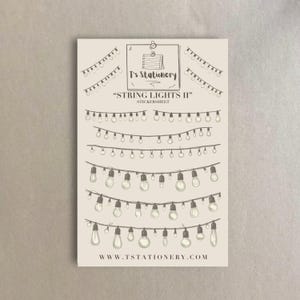 Può includere: Un foglio di adesivi con più file di luci a stringa, ciascuna con un numero diverso di lampadine. Il foglio è intitolato "String Lights II" e ha il sito web "www.tstationery.com" in basso.