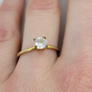 May include: A gold ring with a round, clear gemstone set in a prong setting.