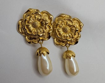May include: Gold flower-shaped earrings with a pearl drop on each earring.
