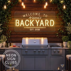 Puede incluir: Un letrero de neón rectangular con iluminación amarilla cálida montado en una pared de madera. El letrero muestra el texto "WELCOME TO Arianna's BACKYARD EST. 2026" en una fuente sans-serif, colocado sobre una parrilla de acero inoxidable.