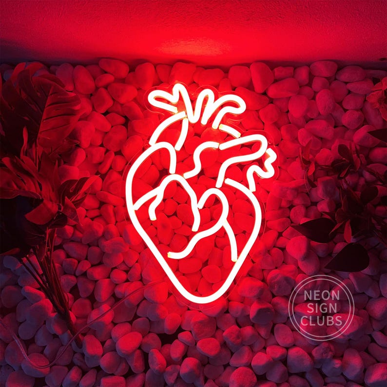 Peut inclure: Enseigne au n&eacute;on blanche en forme de c&oelig;ur humain, sur fond rouge. L'enseigne est fix&eacute;e sur un mur de petits cailloux teint&eacute;s de rouge. Le signe porte le texte "Neon Sign Clubs".
